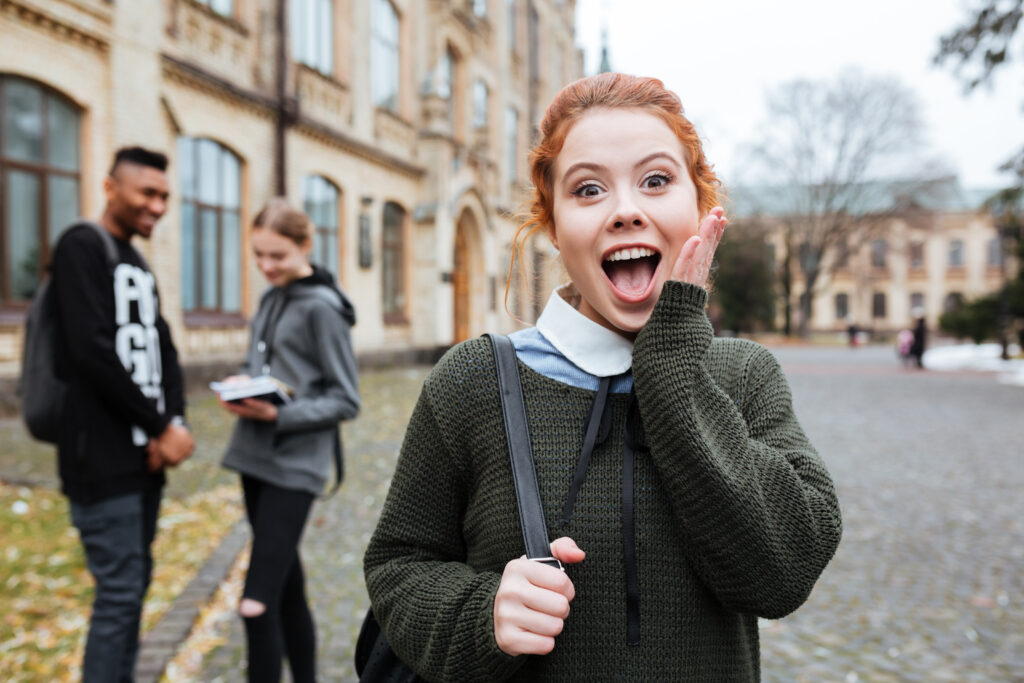 Portrait of an astonished cute teenager with backpack standing at campus