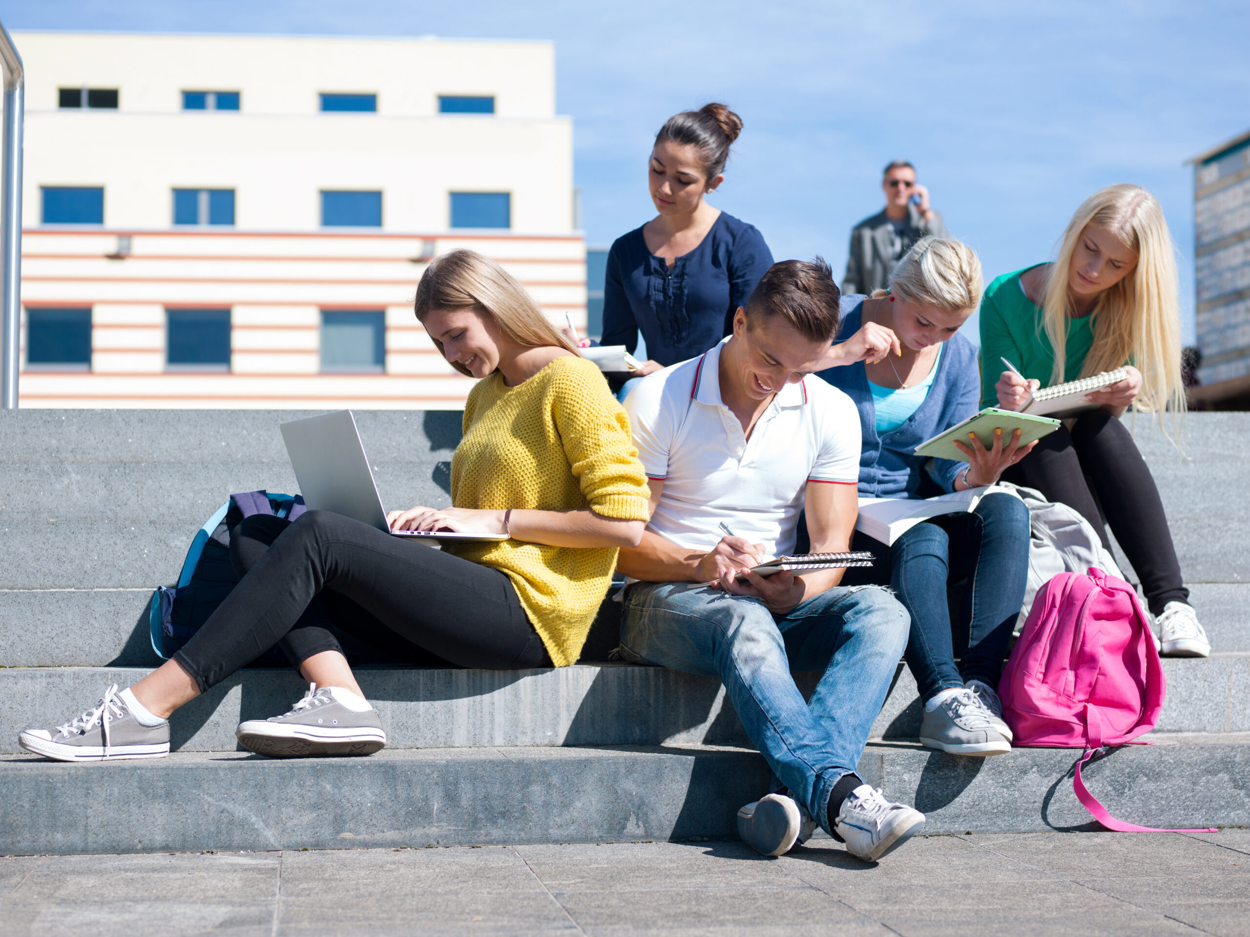 Group portrait of happy students outside sitting on steps have fun